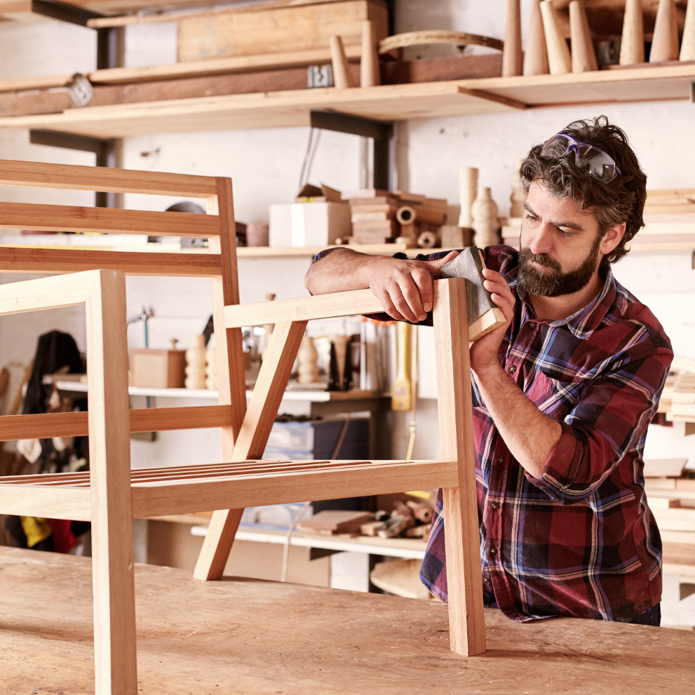 Möbelbauer schleift an Holzstuhl in Möbelwerkstatt